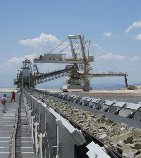 A mining conveyor system transporting rocks with heavy machinery in the background